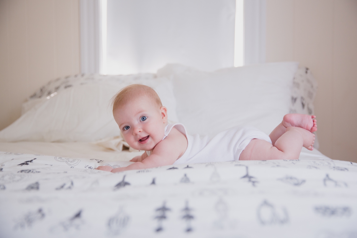 A sweet photograph of a baby girl laying on the bed during an in home family photo session in Boston