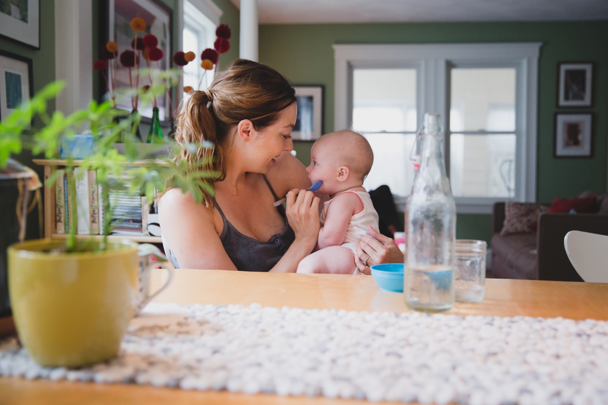 A beautiful photograph of a mother feeding her baby at the table during an in home family photo session in Boston