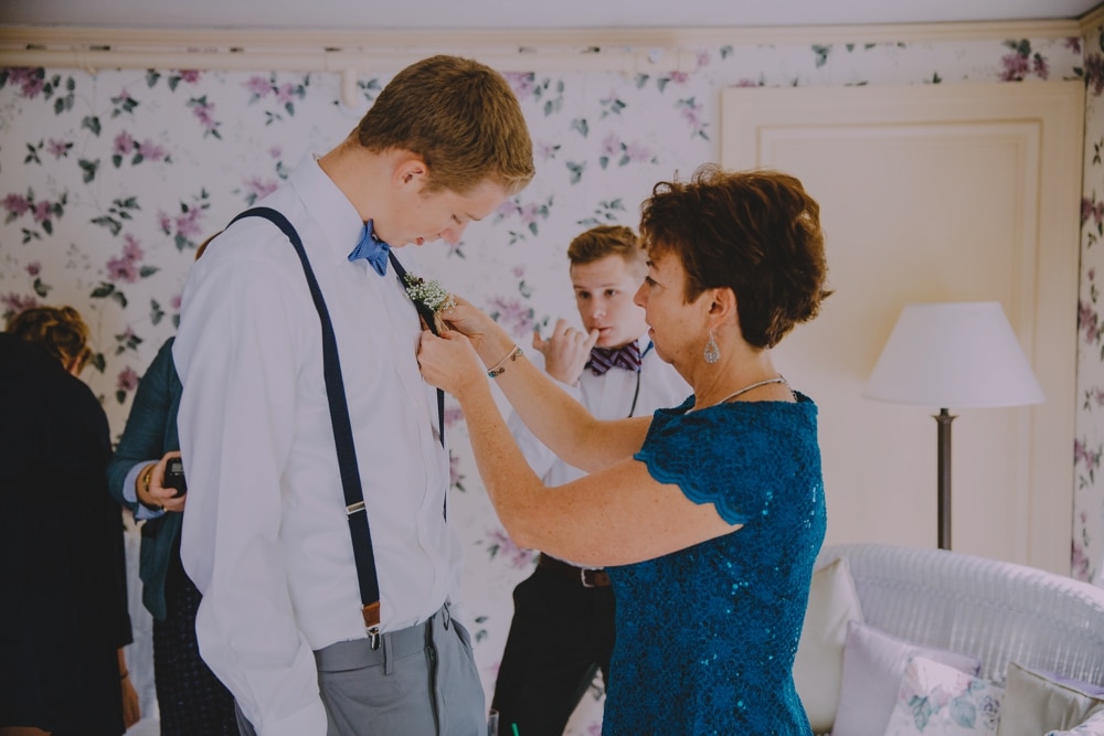 A photojournalistic photograph of a mother putting a boutonnière on her son at the Governors Inn before a rustic barn wedding at Kitz Farm in New Hampshire 