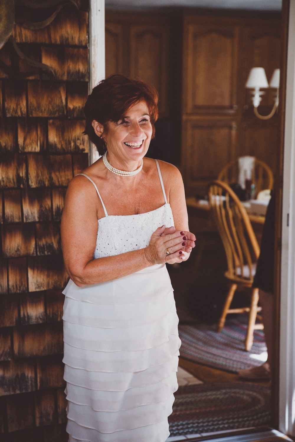 A photojournalistic photograph of a mom smiling as she sees her daughter in her wedding dress before her rustic River Club Wedding in Scituate, Massachusetts