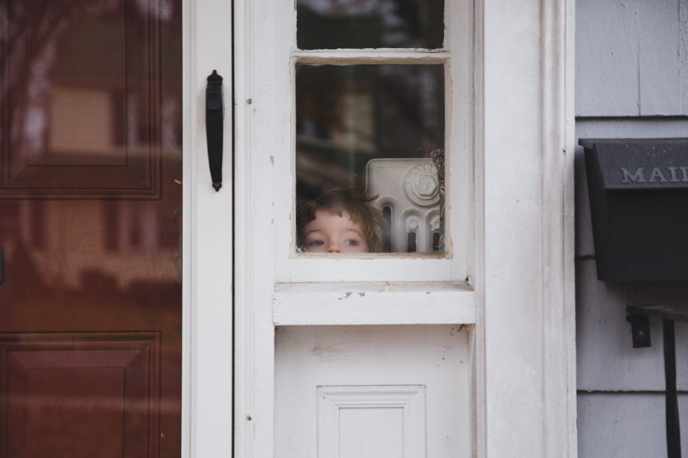 A documentary photograph of a little boy looking out the window during an in home family session in Boston, Massachusetts