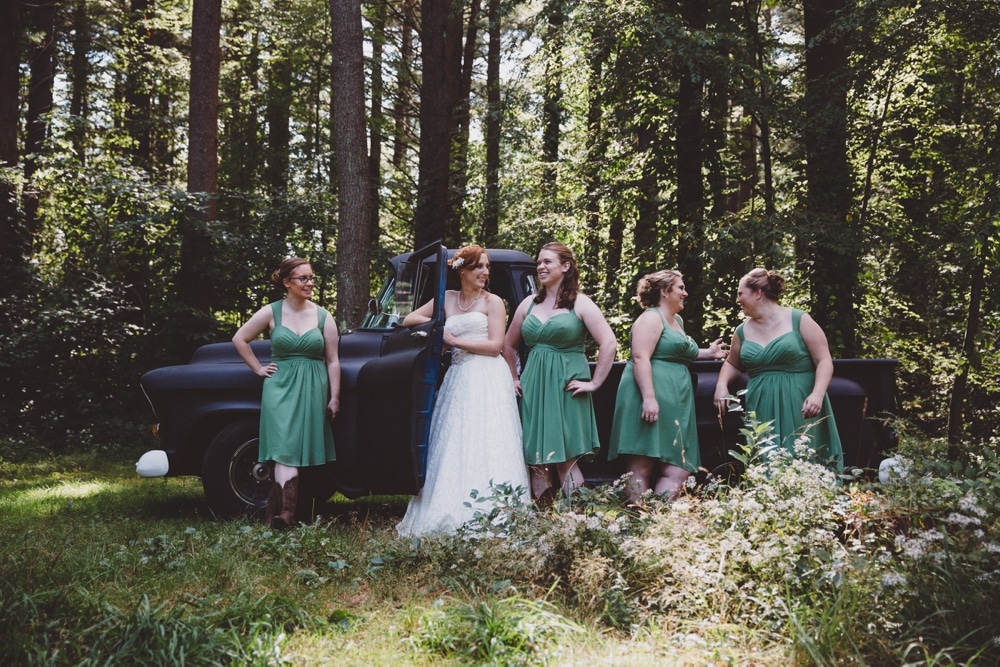 A natural and relaxed portrait of a bride and her bridesmaids in the woods with a vintage Chevrolet truck during a rustic River Club Wedding in Scituate, Massachusetts
