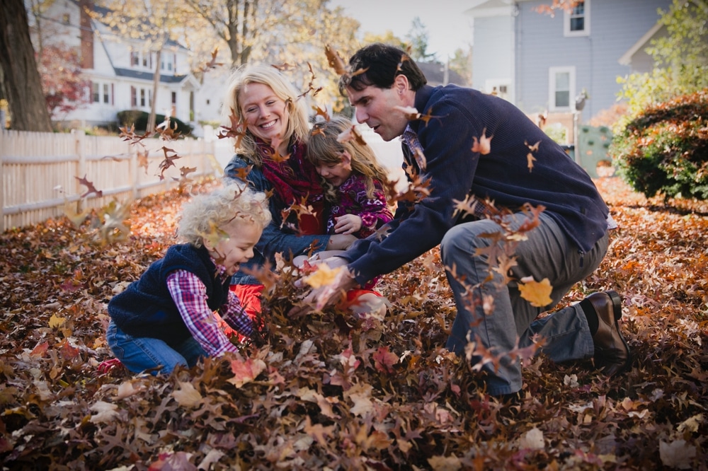 A lifestyle photograph of a family playing in the fallen leaves during their in home session in Boston, Massachusetts