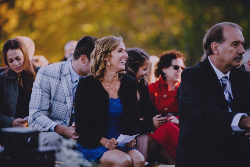 A documentary photograph of wedding guests laughing during a rustic outdoor New Hampshire wedding ceremony at Kitz Farm