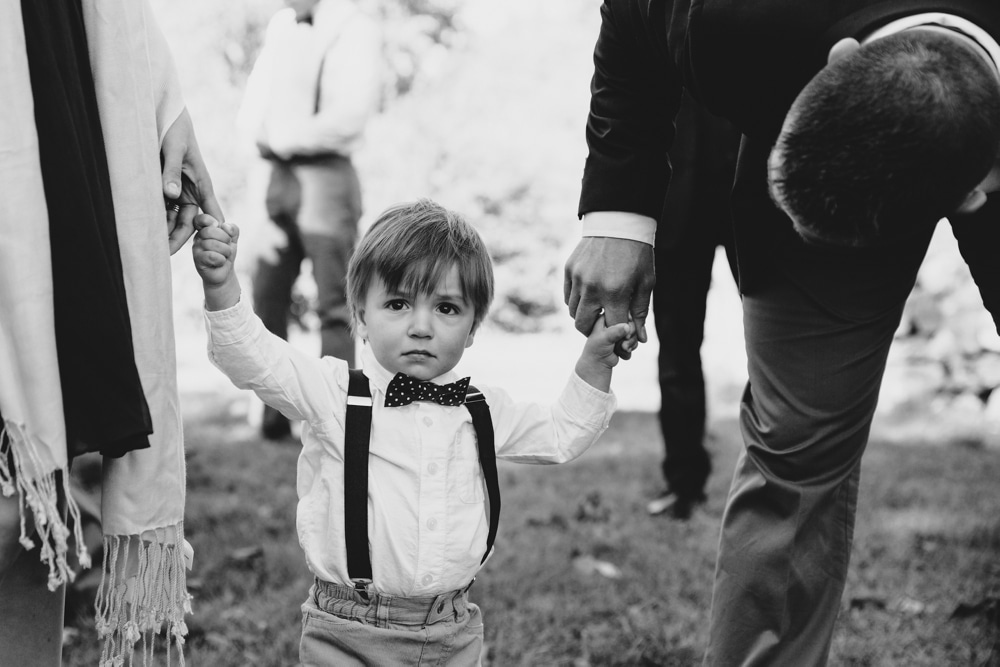 A photojournalistic photograph of a ring bearer moments before he walks down of the aisle during a rustic outdoor Kitz Farm wedding ceremony in New Hampshire