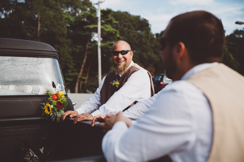 A photojournalistic photograph of groomsmen talking and laughing during a rustic River Club Wedding in Scituate, Massachusetts