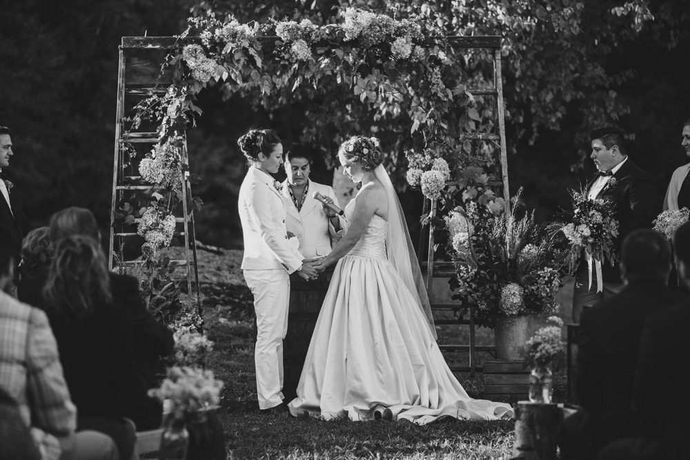 A documentary photograph of two brides reading their vows during a rustic outdoor wedding ceremony in the fall at Kitz Farm in New Hampshire