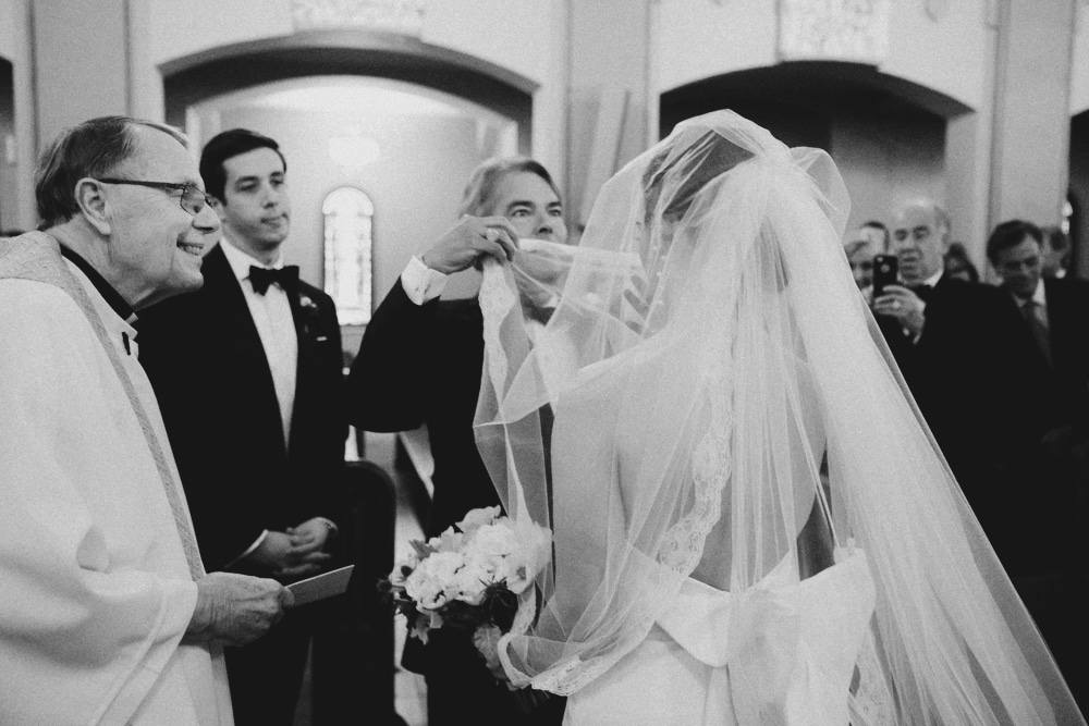 A documentary photograph of a father lifting the veil of his daughter during her church wedding ceremony in newport, rhode island