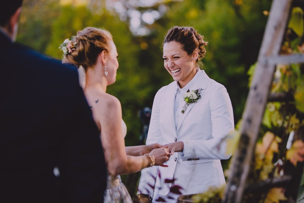 An emotional documentary photograph of two brides smiling as they exchange rings during their rustic fall outdoor wedding ceremony at Kitz Farm in New Hampshire