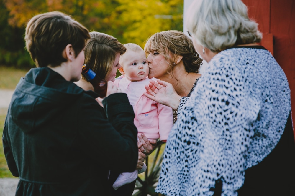 A documentary photograph of wedding guests kissing and hugging a baby during a rustic New Hampshire barn wedding at Kitz Farm