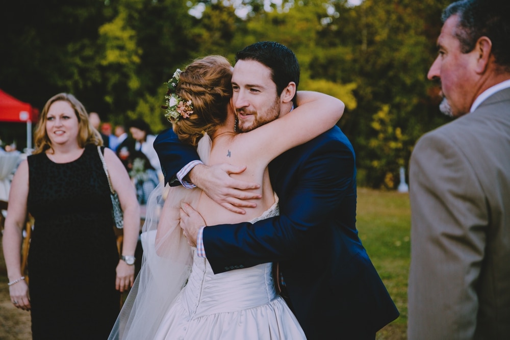 A photojournalistic photograph of a bride hugging a wedding guest during her laid back rustic wedding reception at Kitz Farm in New Hampshire