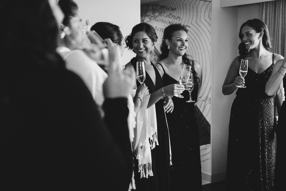A photojournalistic photograph of bridesmaids having a glass of champagne while getting ready at the Hyatt Regency Hotel before a wedding at the Castle Hill Inn in Newport, Rhode Island