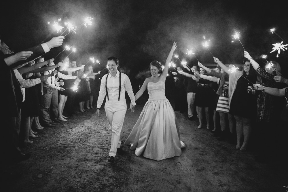 A documentary photograph of a bride and bride laughing during the sparkler exit of their rustic barn wedding at Kitz Farm in New Hampshire