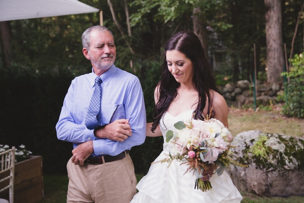 A documentary photograph of a father looking at his daughter as they walk up the aisle during her backyard wedding ceremony in Boston, Massachusetts