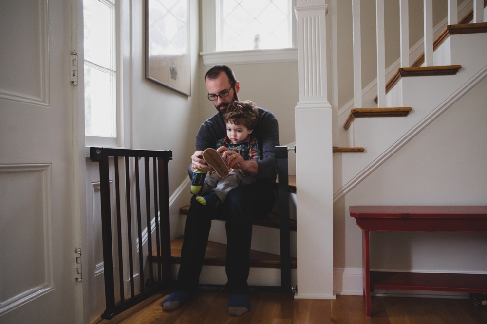 A documentary photograph of a father putting on his sons shoes during a in home lifestyle family photo session in Boston, Massachusetts