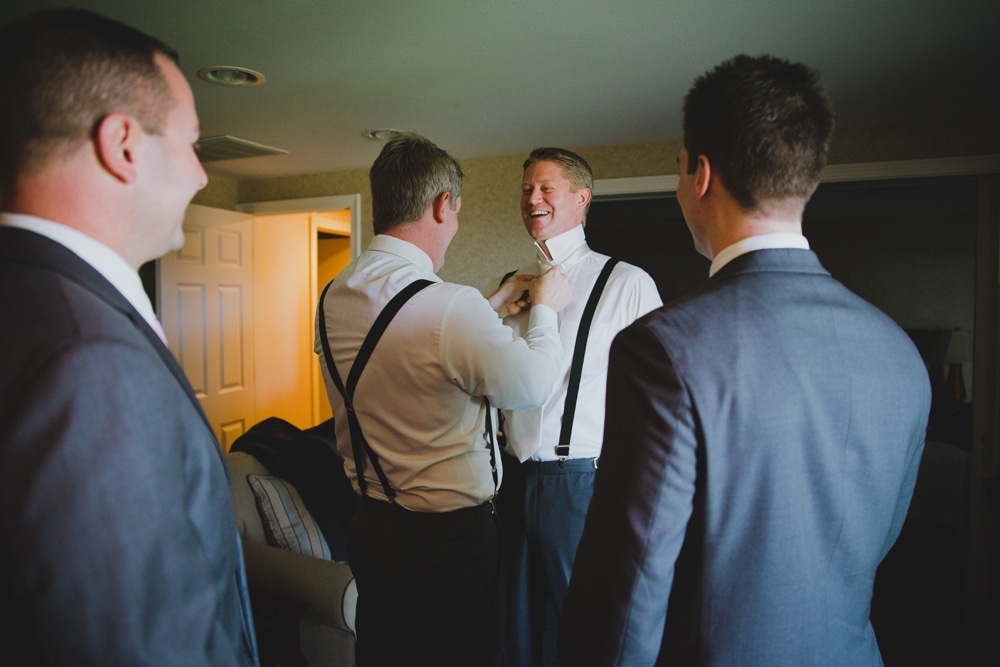 A photojournalistic photograph of a best man helping the groom put on his tie during a fun wedding in Cape Cod