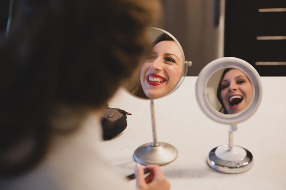 A photojournalistic photograph of a bride and bridesmaids looking in the mirror while they get ready for a Massachusetts wedding at the Oceanview of Nahant