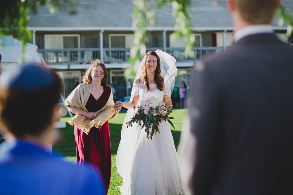A documentary photograph of a bride walking up the aisle with mother during an outdoor wedding ceremony in Cape Cod, Massachusetts