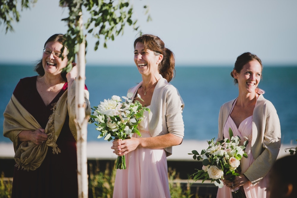 A documentary photograph of bridesmaids laughing during an outdoor jewish wedding ceremony in Cape Cod, Massachusetts