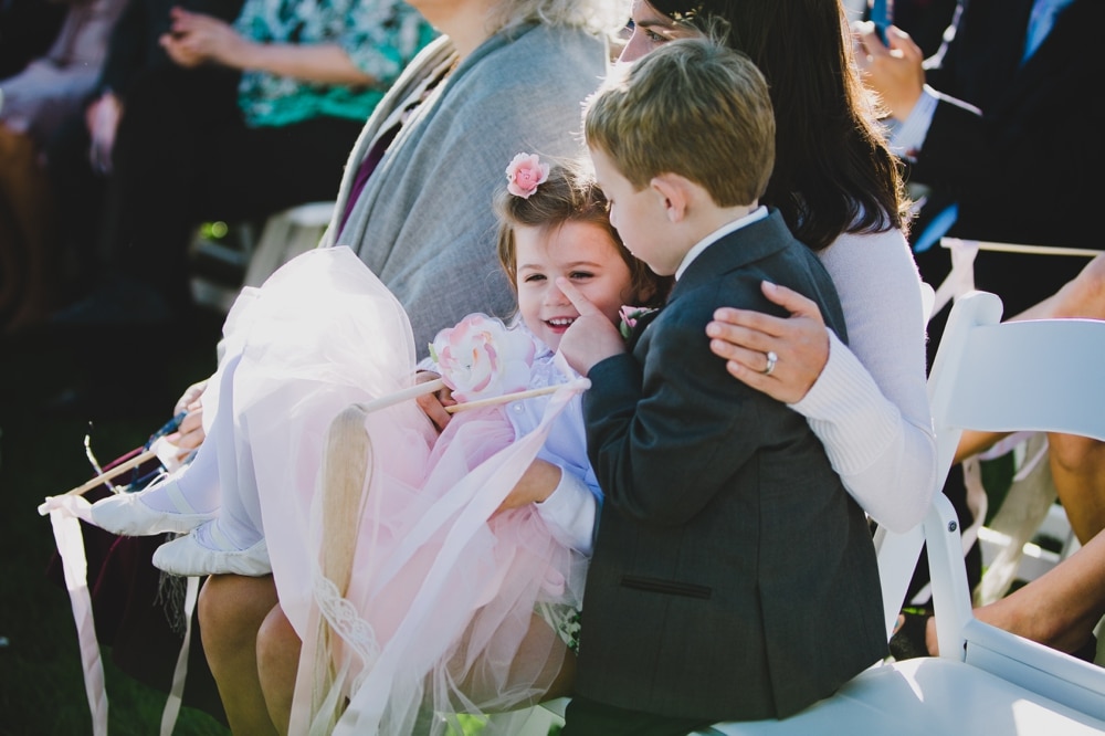 A documentary photograph of a ring bearer and flower girl playing and laughing during an outdoor Jewish wedding ceremony in Cape Cod, Massachusetts