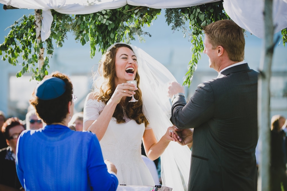 A documentary photograph of a bride and groom laughing during an outdoor Jewish wedding ceremony in Cape Cod, Massachusetts