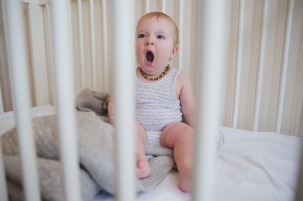 A photojournalistic photograph of a baby girl yawning in her crib during an in home lifestyle session in Boston