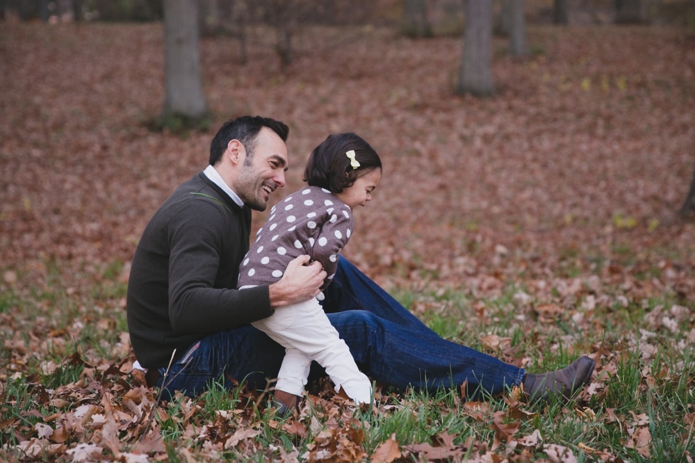 A lifestyle photograph of a father playing with his daughter during their fall mini session at the Arnold Arboretum in Boston, Massachusetts