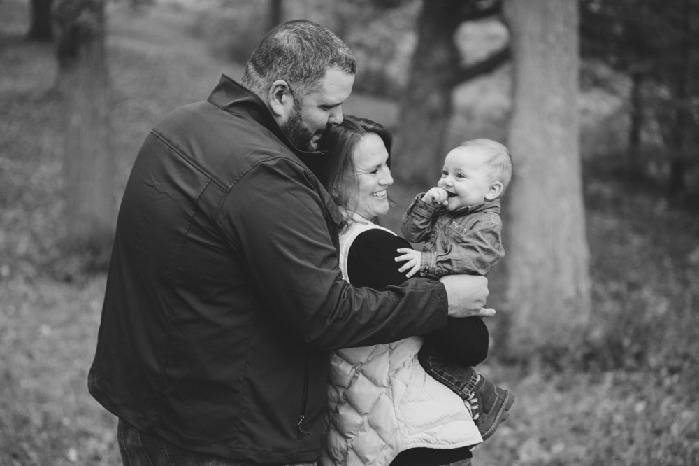 A lifestyle photograph of parents holding their baby boy during a fall family mini session at the Arnold Arboretum in Boston, Massachusetts