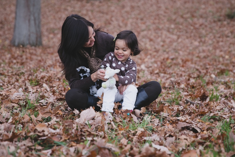 A lifestyle photograph of a mother playing with her daughter during their fall mini session at the Arnold Arboretum in Boston, Massachusetts
