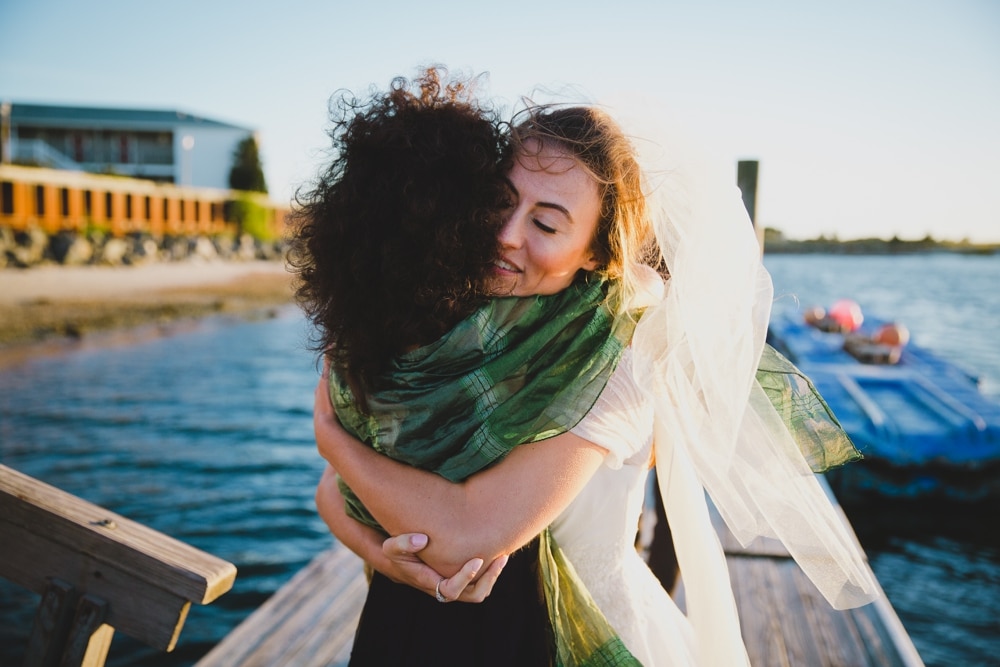 A documentary photograph of a bride hugging her friend just moments after her Jewish wedding ceremony on Cape Cod