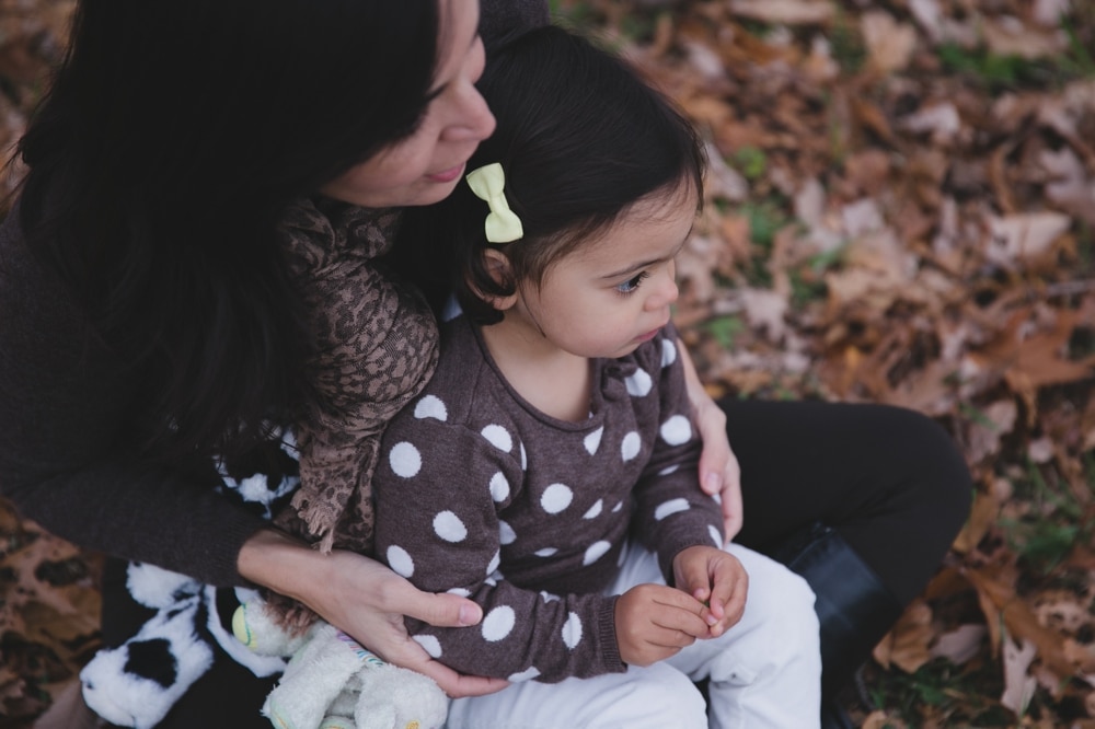 A lifestyle portrait of a daughter sitting on her mother's lap during a fall mini session at the Arnold Arboretum in Boston, Massachusetts