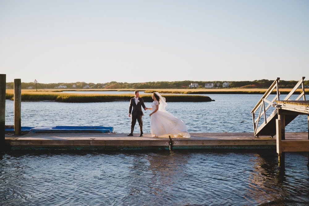 A documentary photograph of bride and groom walking on a jetty during their summer wedding on Cape Cod