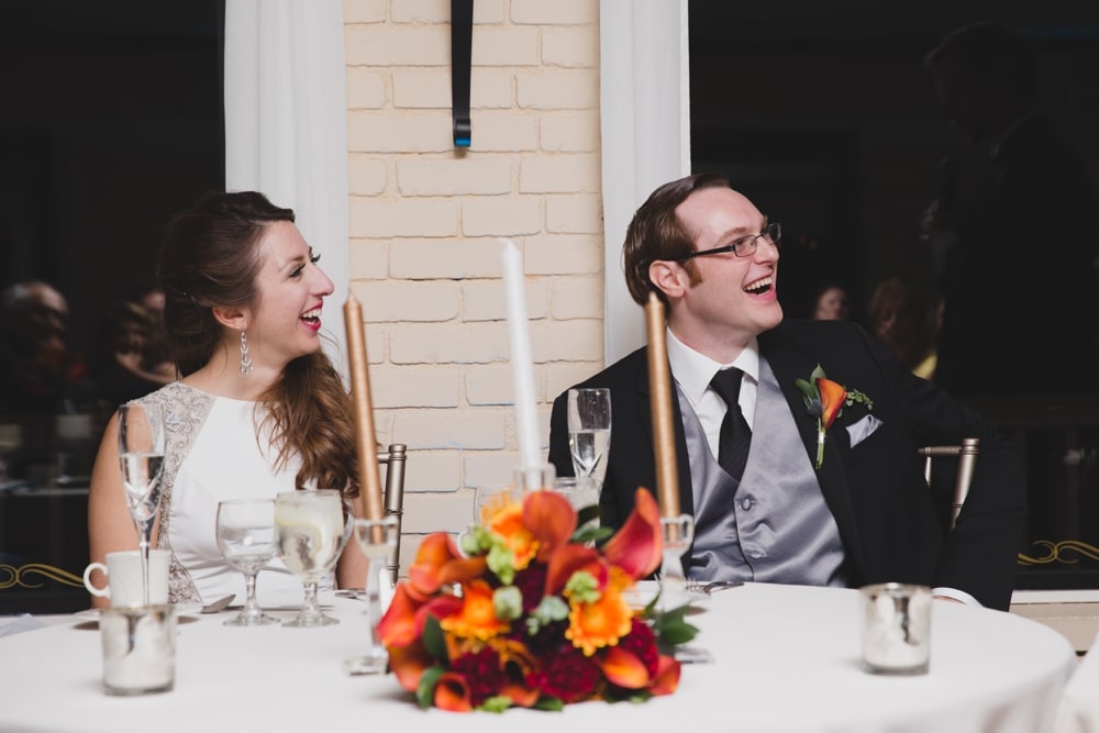 A documentary photograph of a bride and groom laughing during the best man speech during their intimate Massachusetts wedding at the Oceanview of Nahant