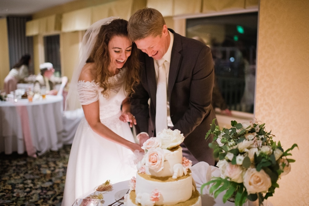 A photojournalistic photograph of a bride and groom cutting the cake at their summer wedding on Cape Cod