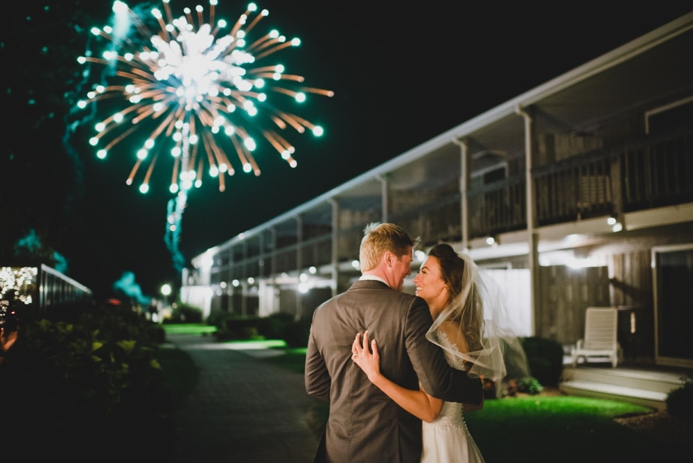 A documentary photograph of a bride and groom looking at each other during a fireworks display at their summer time wedding in Cape Cod