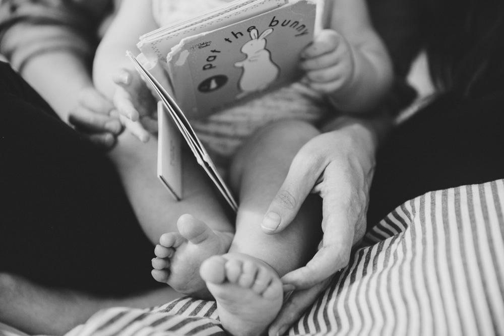 A documentary photograph of a mother reading a book to her baby girl during their in home lifestyle session in Boston