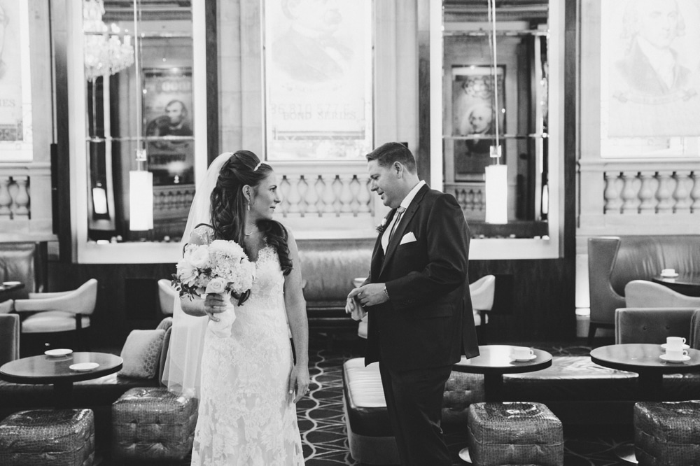 A documentary photograph of a groom checking out his bride during their first look at the Bond Lounge in the Langham Hotel before their State Room Wedding in Boston
