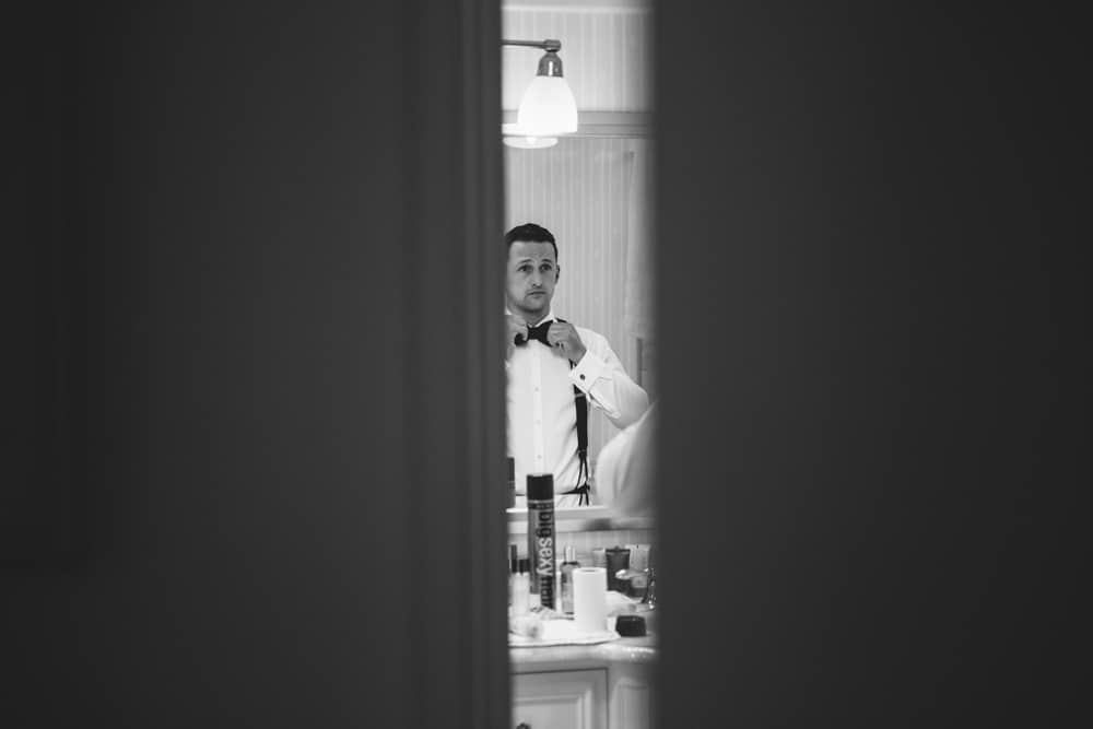 A documentary photograph of groom tying his bow tie in the bathroom before his Taj Boston Hotel Wedding in the Back Bay