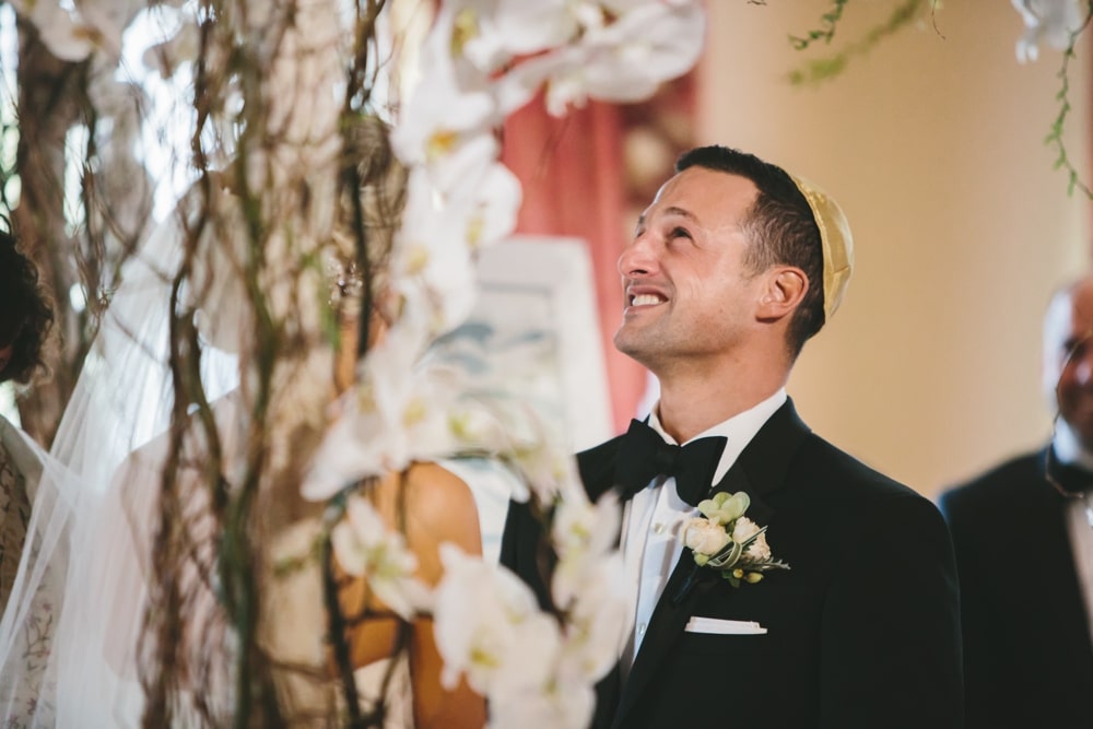 A documentary photograph of a groom smiling as his bride says her vows during their Taj Boston Hotel Wedding in the Back Bay