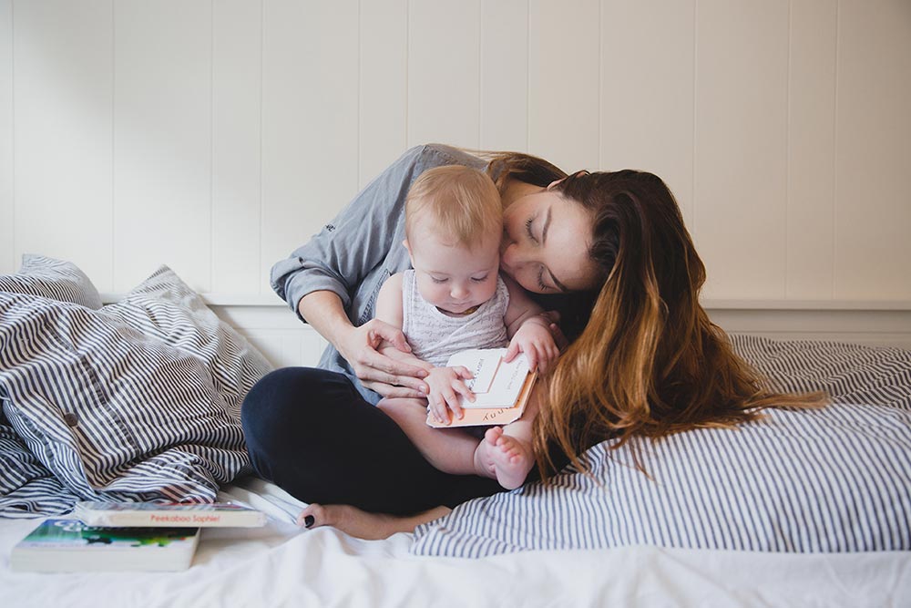 A lifestyle photograph of a mother reading a book to her baby during an in home family session in Boston