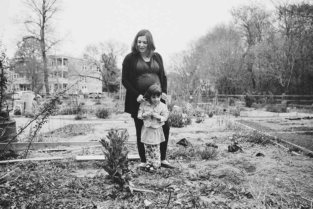 A documentary photograph depicting everyday motherhood as a pregnant mother and her daughter look at the garden near the Boston home during a lifestyle family session