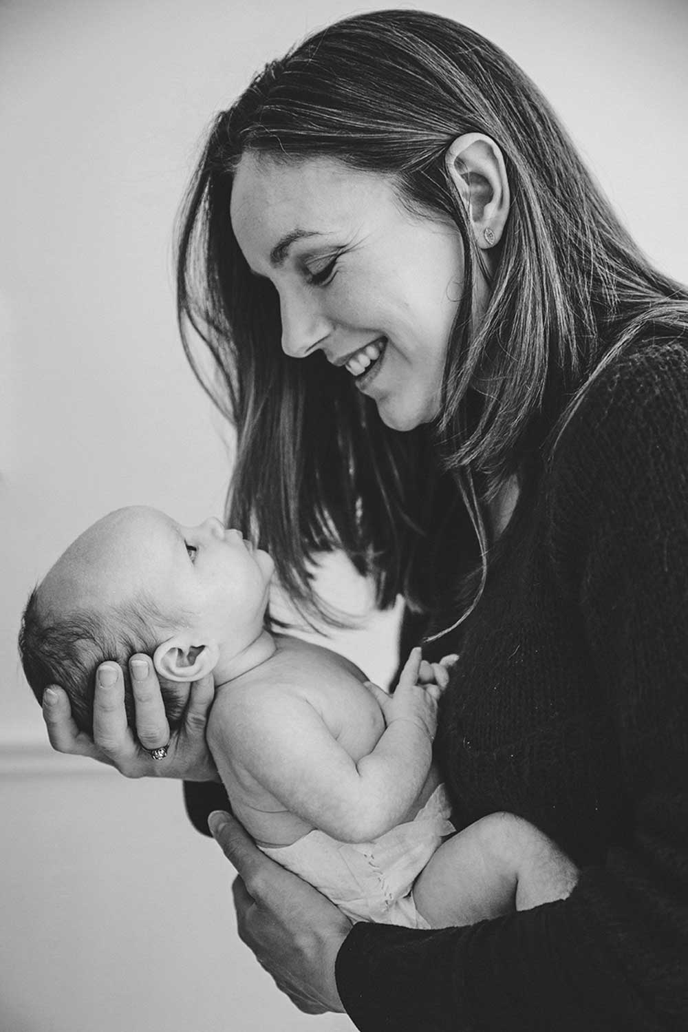 A lifestyle photograph of everyday motherhood as a new mom smiles at her newborn daughter during an in home family session in Boston