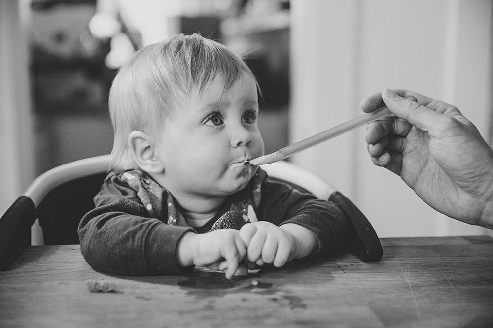 A lifestyle photograph of a baby boy eating yogurt during a family session at home in Boston, Massachusetts