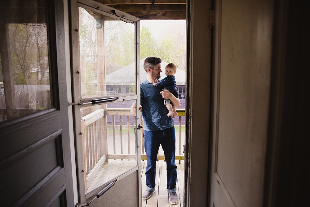 A documentary photograph of a father holding his son as they walk outside during a family session at home in Boston, Massachusetts