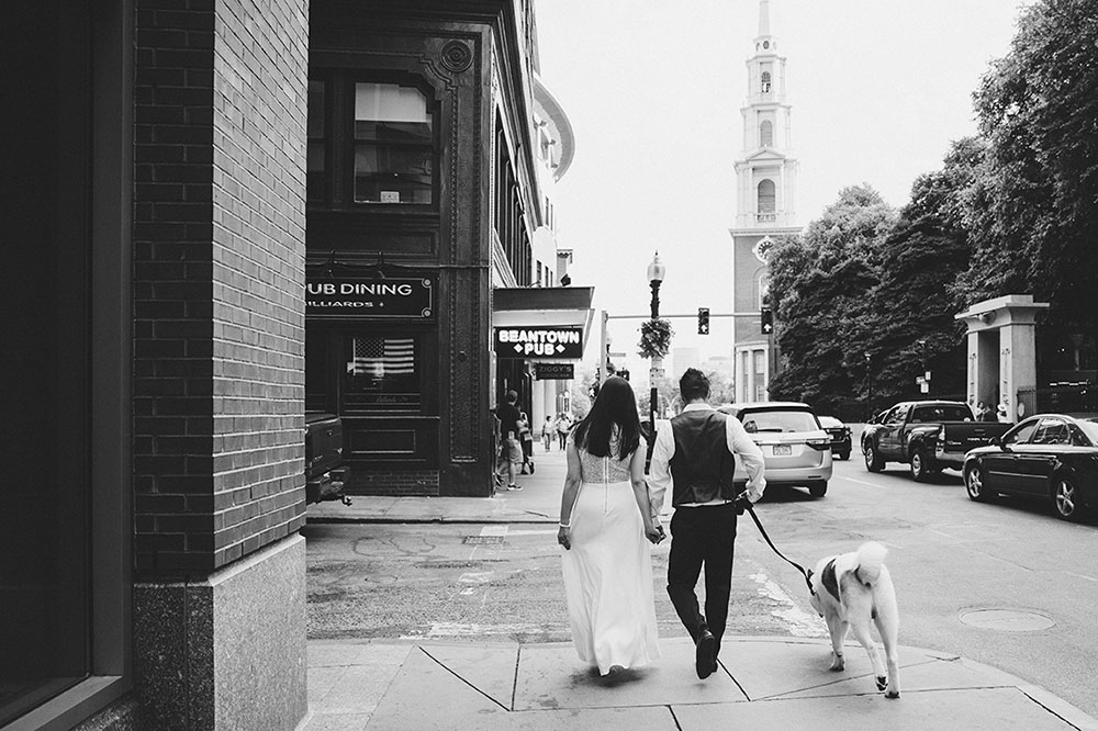 A documentary photograph of a couple walking through the city with their dog during their Boston Engagement Session