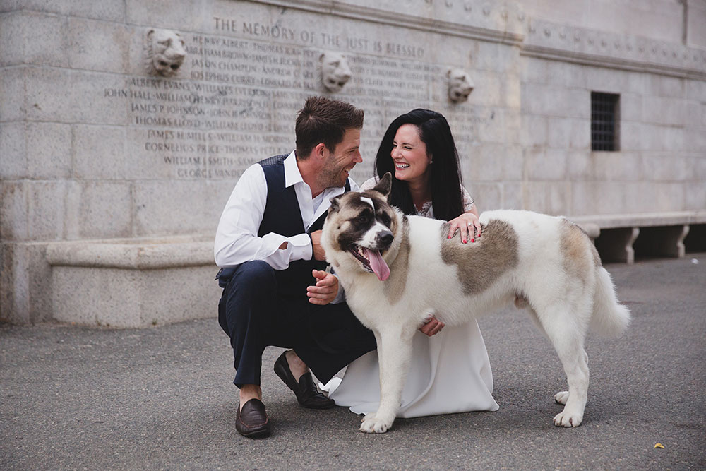 A documentary photograph of couple petting their dog and laughing in Boston Common during their Boston Engagement Session