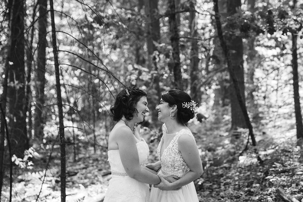 A documentary photograph of two brides smiling during the first look at their Friendly Crossways Wedding
