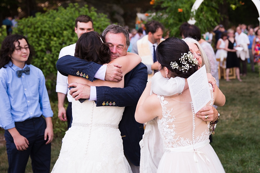 A documentary photograph of two brides hugging their parents after their outdoor wedding ceremony at Friendly Crossways