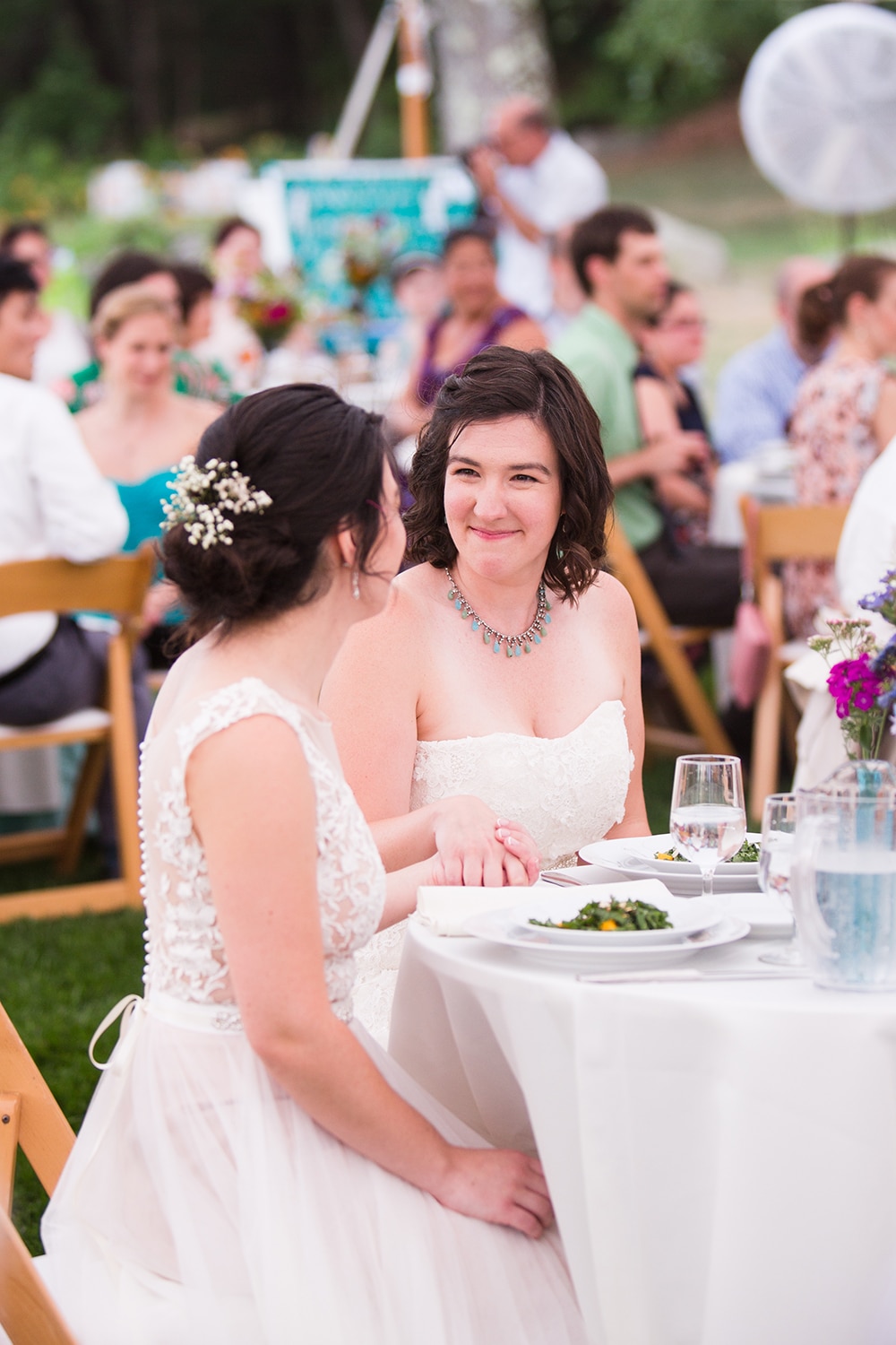 A documentary photograph of two brides looking at one another during the toasts at their Friendly Crossways Wedding