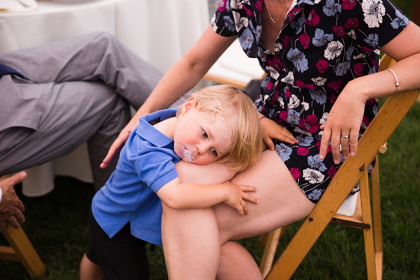 A documentary photograph of a toddler resting on his mother's knee during a Friendly Crossways Wedding